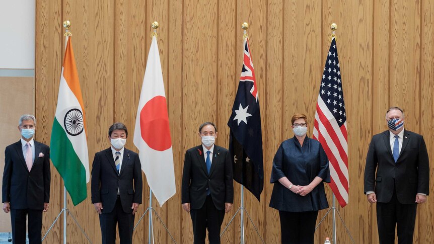 The five members of the Quad, and the Japanese PM, standing in a row behind their respective flags