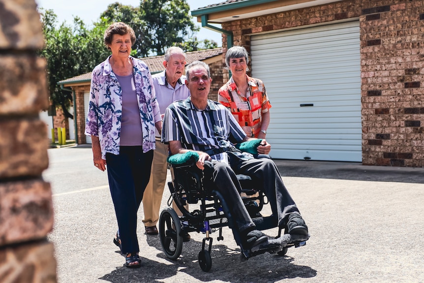 a family pushing a man on a wheelchair out near houses