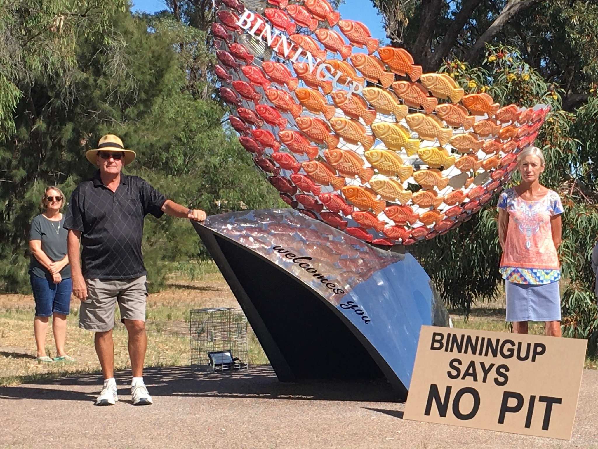two women and a man standing apart, in front of the Binningup entrance with a sign that says 'Binningup says no pit".