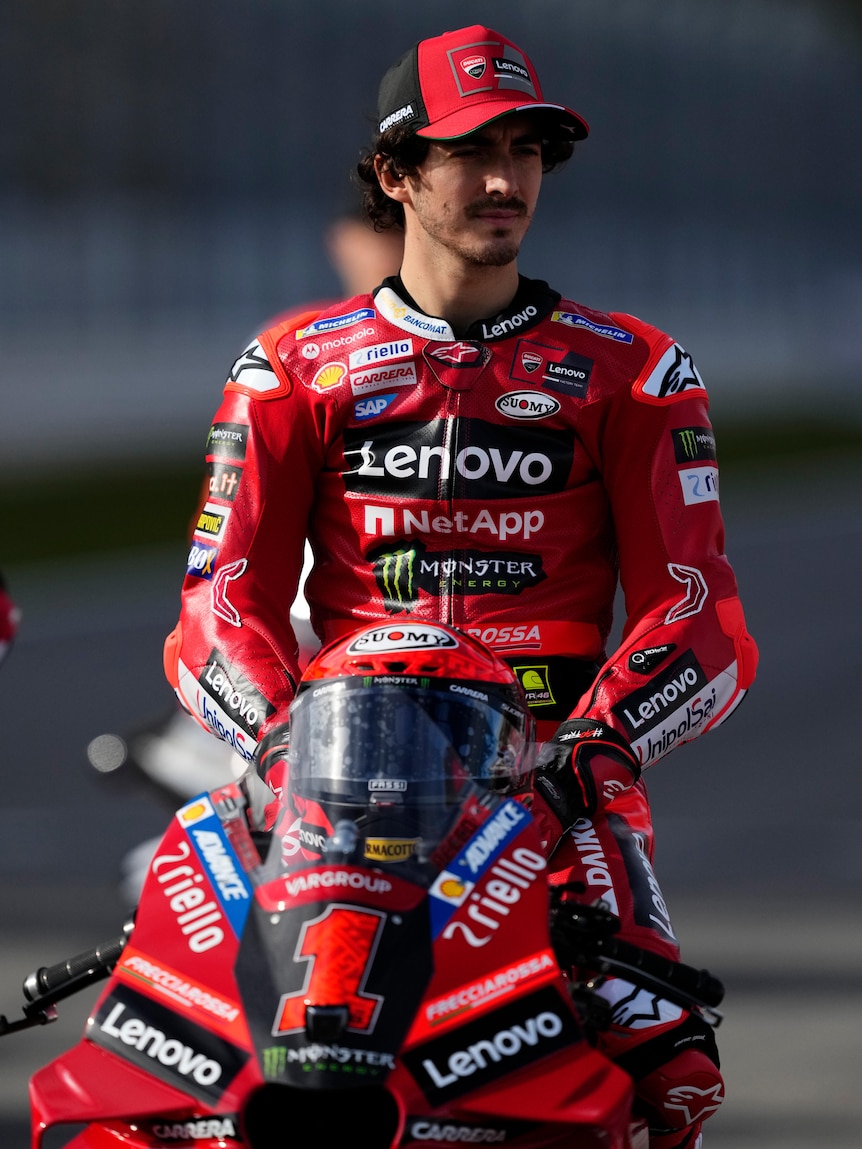 Pecco Bagnaia sits on a motorbike in red leathers with his helmet off