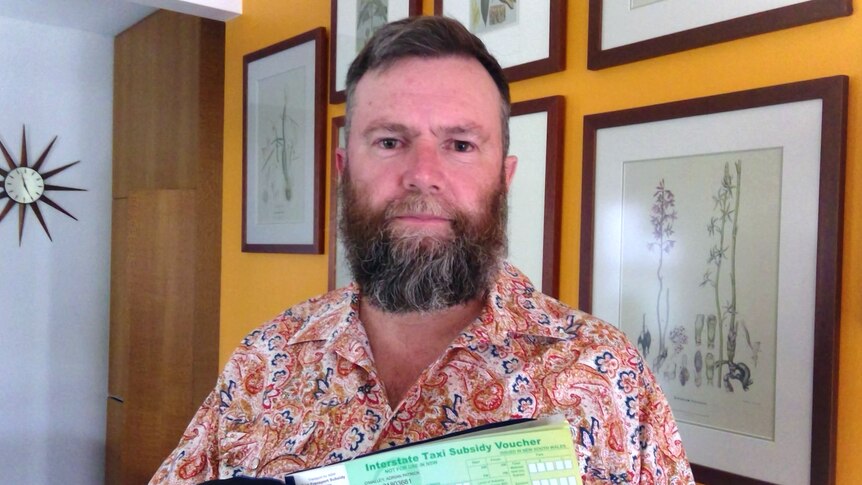 A middle-aged man with a beard holds up a small booklet with vouchers in it
