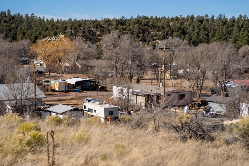 A view from a hill of a little trailer park with dried out trees and grass and old buildings