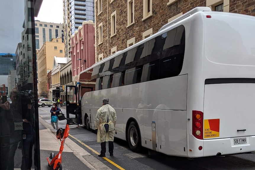 A bus in a laneway with old stone buildings and people wearing PPE