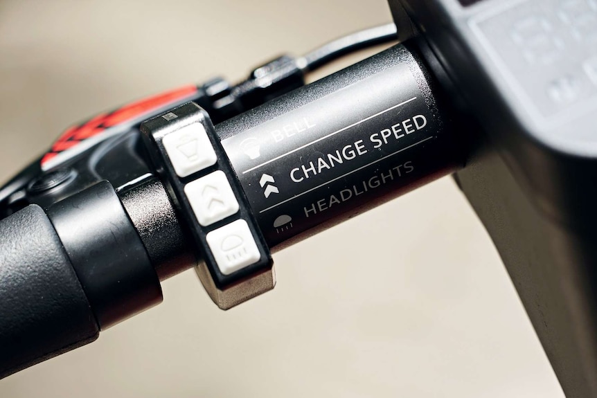 A close-up shot of a Neuron e-scooter handle showing buttons for a bell, headlights and changing speed.
