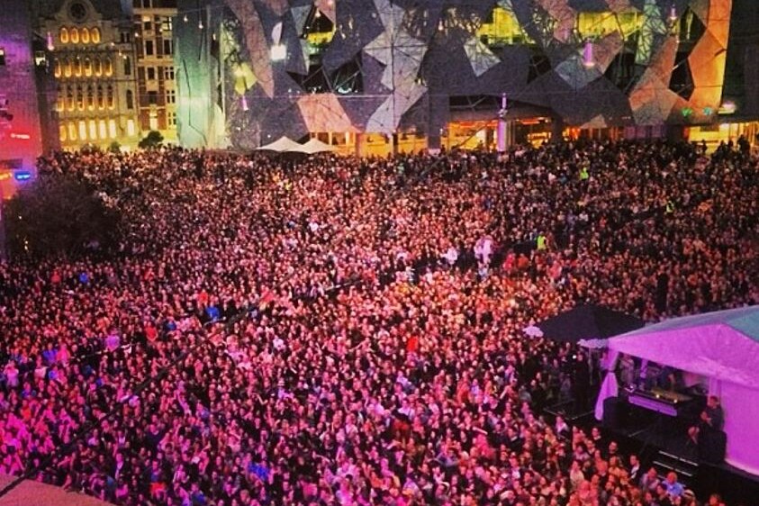 At night, a bird's eye view of huge crowd packed into outdoor area surrounding the the FedSquare building.