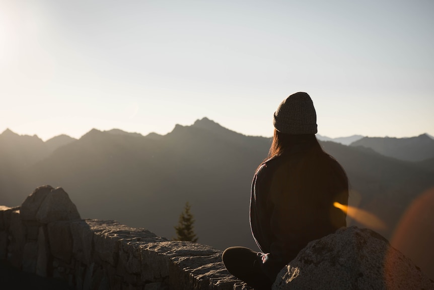 Back of a woman who is sitting on rocks, looking at mountains.