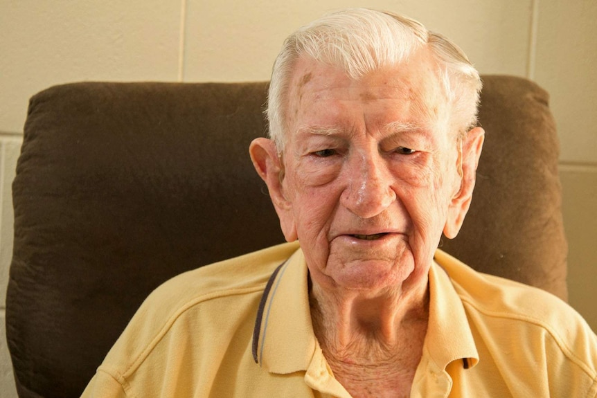 An elderly man with hearing aids sits in a comfy chair