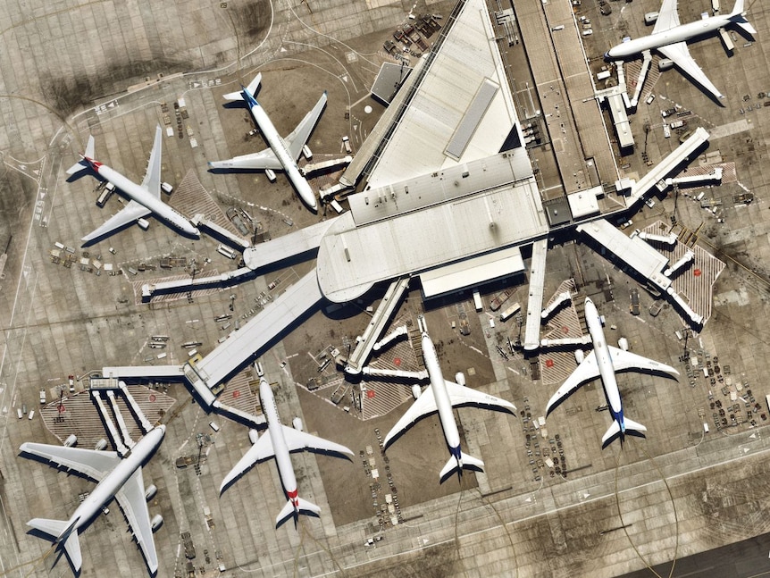 A terminal and several large planes at Sydney Airport, seen topdown from space.