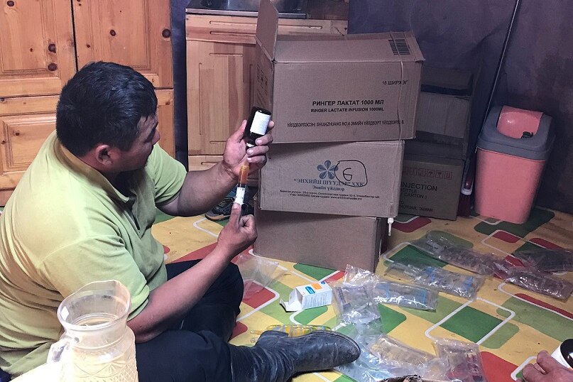 A man sits on the floor and fills a large syringe with performance enhancing drugs from a bottle.