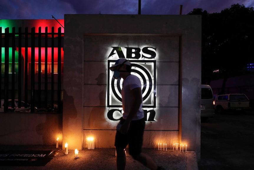 The silhouette of a man shadows a neon sign reading ABS-CBN