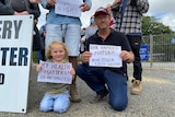 A child and a man hold signs up protesting the approval of a lead battery secondary smelter in their community