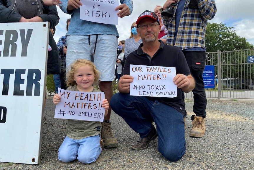 A child and a man hold signs up protesting the approval of a lead battery secondary smelter in their community