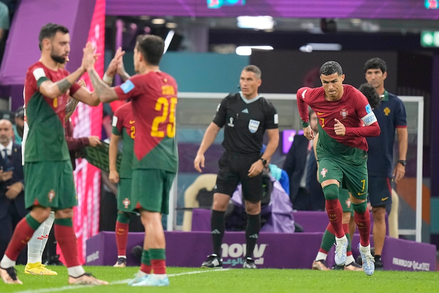 Cristiano Ronaldo runs onto the field during Portugal's win over Spain at the Qatar FIFA World Cup. Two other players high-five.