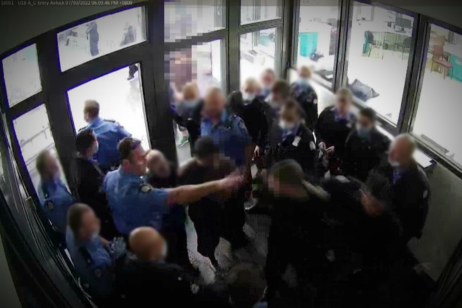 A screenshot of grainy CCTV vision showing dozens of people standing insight a tight space