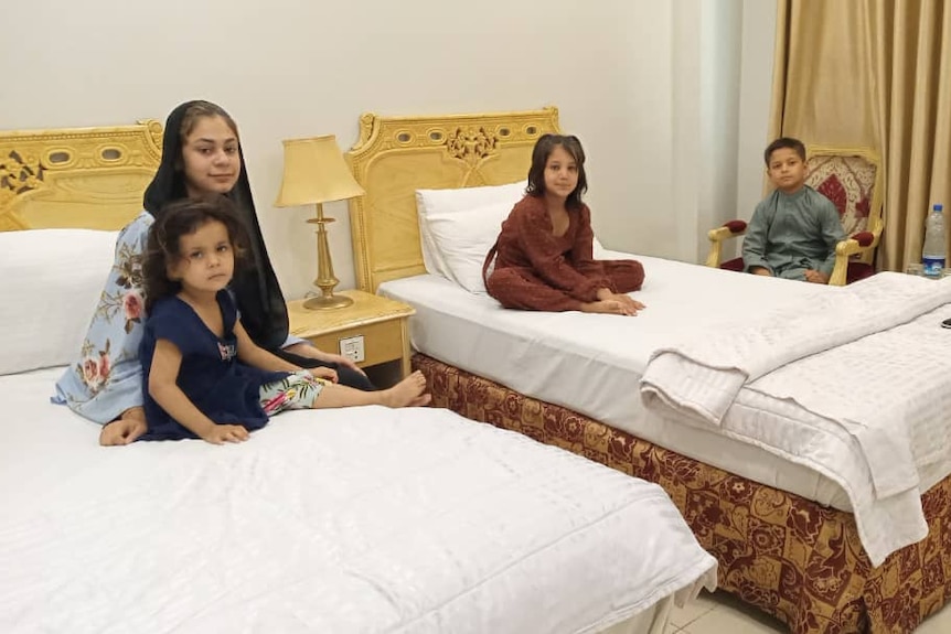 Four children sit on hotel beds. 