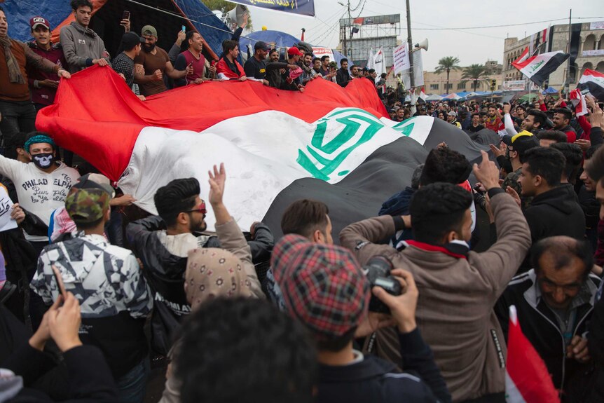 protesters carry a large Iraqi flag and wave smaller flags