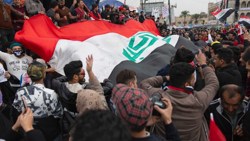 protesters carry a large Iraqi flag and wave smaller flags