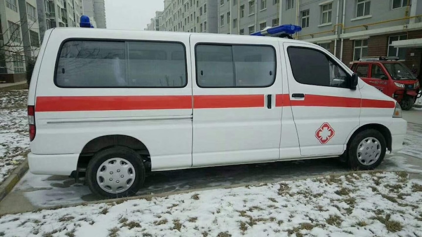 A Chinese ambulance stands in the snow with apartment rows on either side.