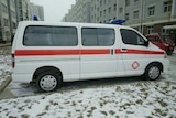 A Chinese ambulance stands in the snow with apartment rows on either side.