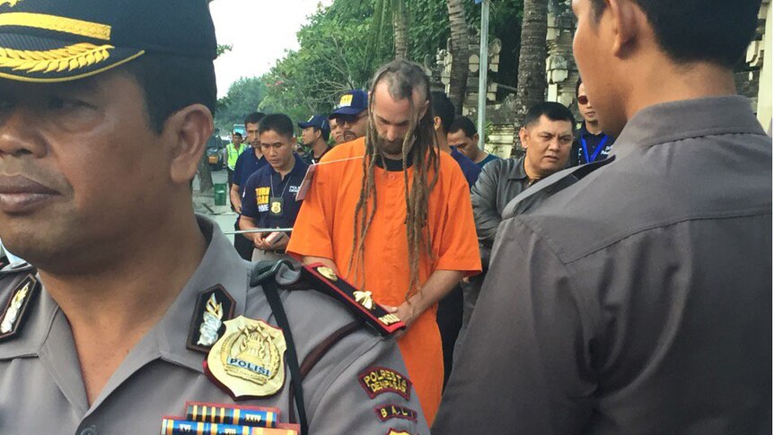 Murder accused David Taylor wearing an orange jumpsuit, surrounded by officials as police lead him through Kuta Beach.