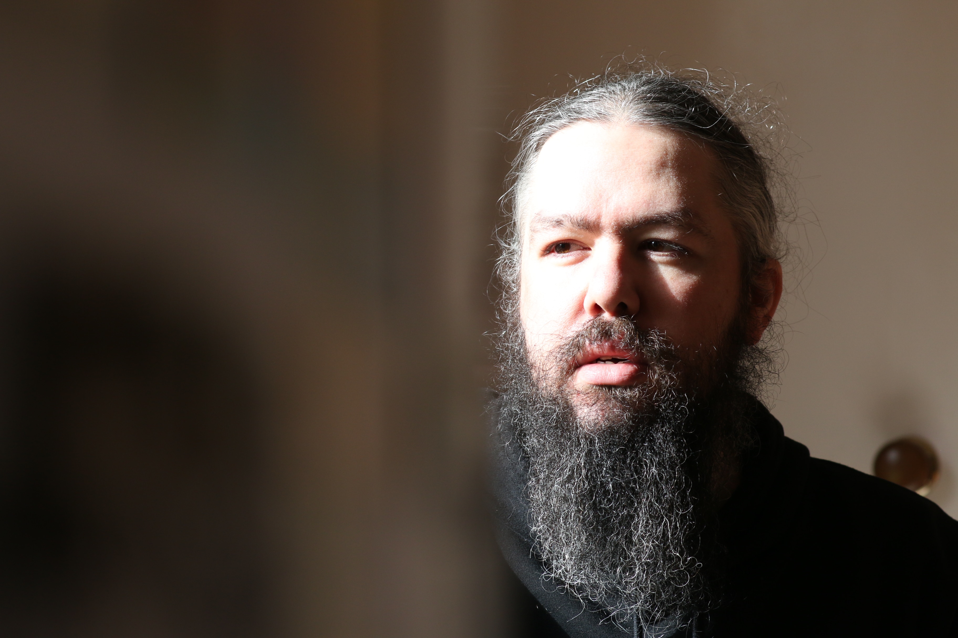 A man with long hair and a long beard looking out the window