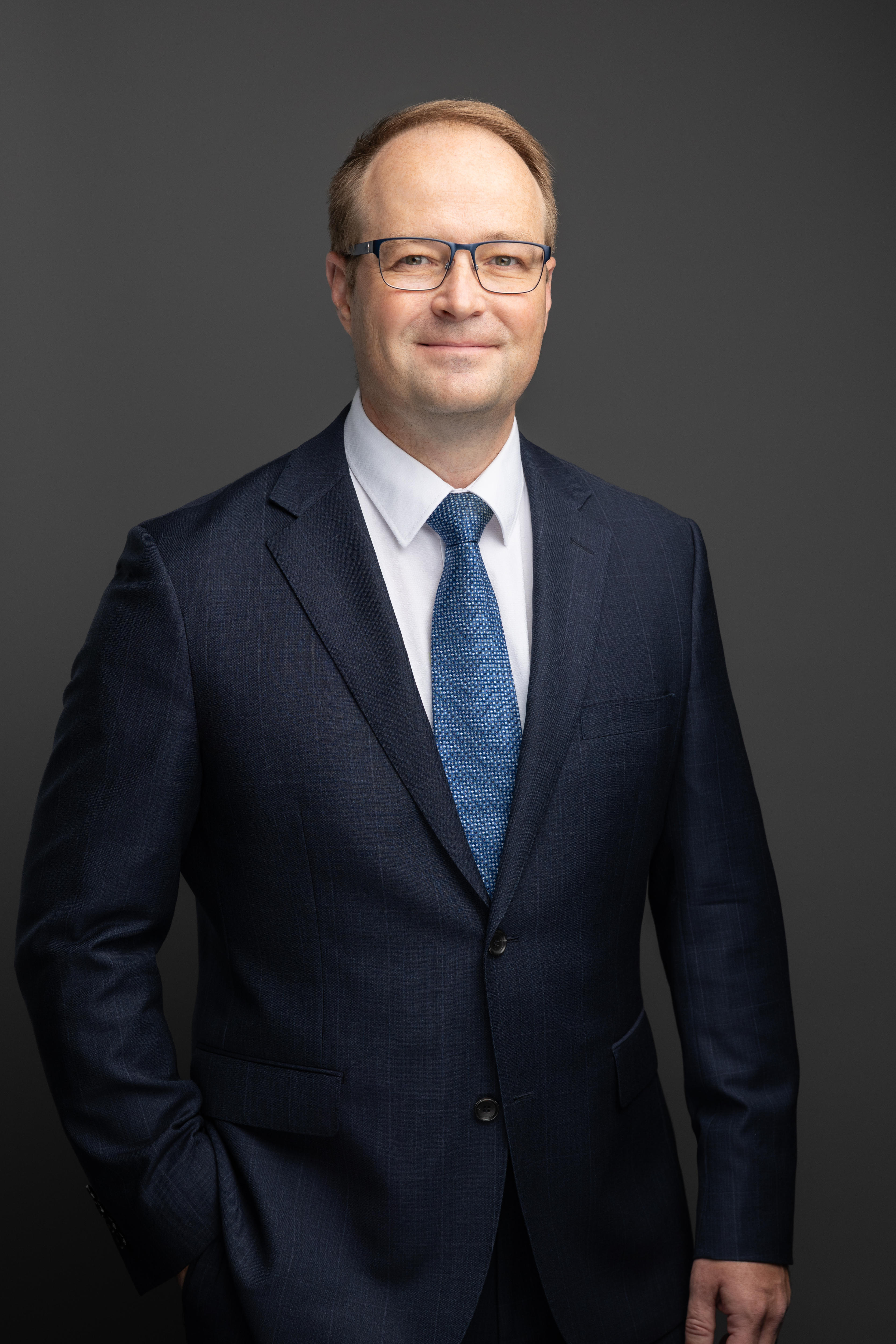 A man with glasses dressed in a suit smiling at the camera. 