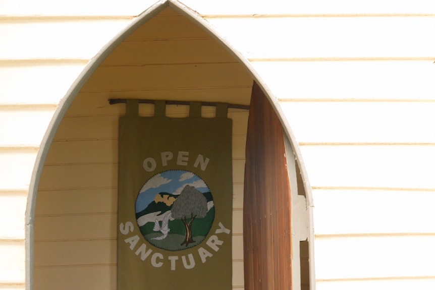 A doorway of a timber church has the word 'open sanctuary' on it