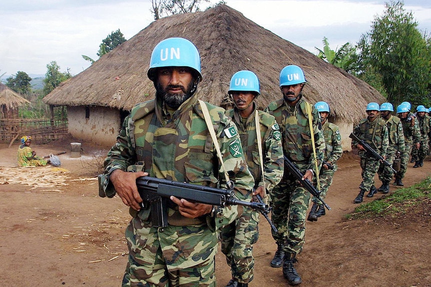 A line of soliders with blue helmets pass through a small African village