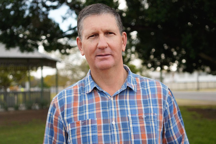 A middle-aged man with short, dark hair, standing outside.