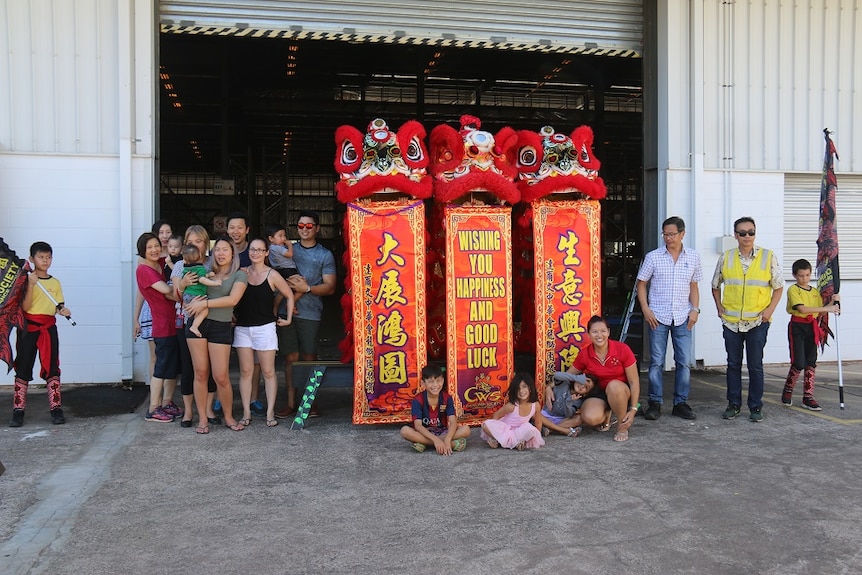 Three Chinese dragons and about 20 people gather outside a warehouse