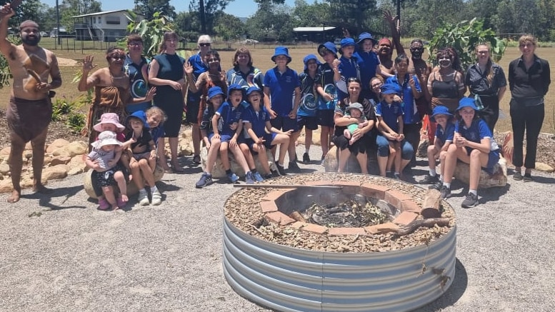 Student and first nations people dressed in traditional attire gather around a firepit.