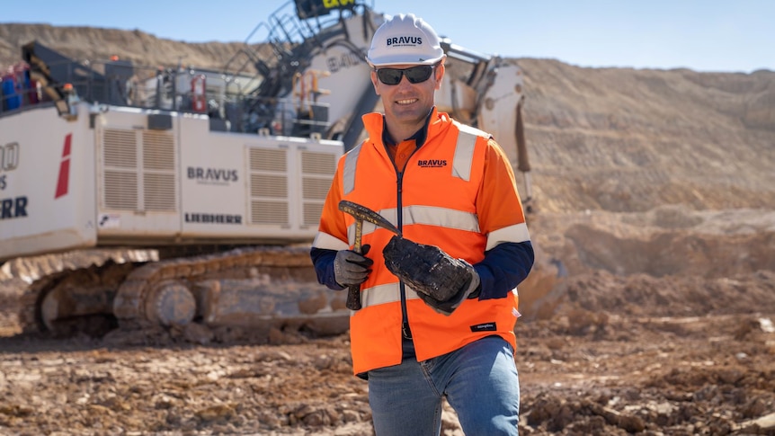 A man stands in an open cut coal mine holding a piece of coal.