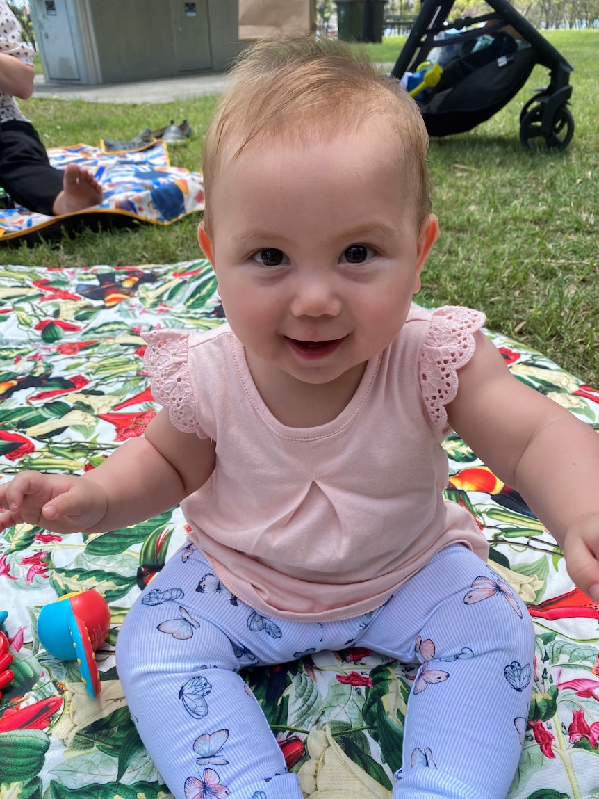A smiling baby sits on a picnic rug