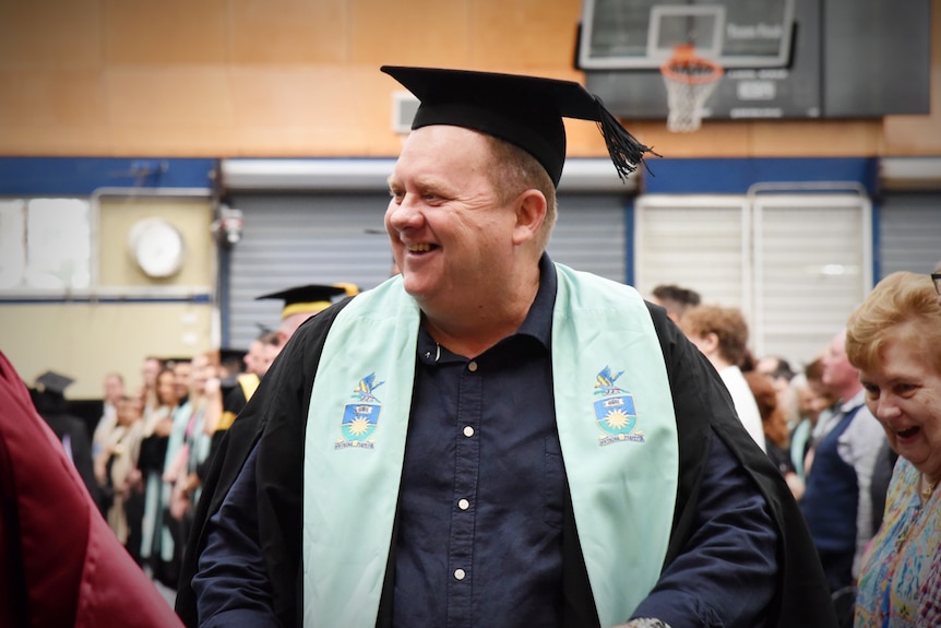 A man in a graduation cap and gown smiling and walking