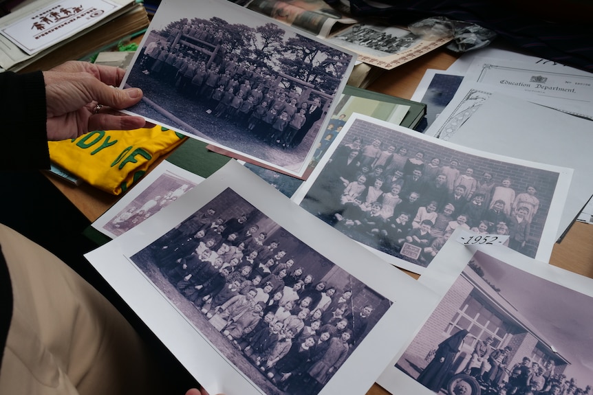 Hands hold historical school photos above a table covered with more photos.