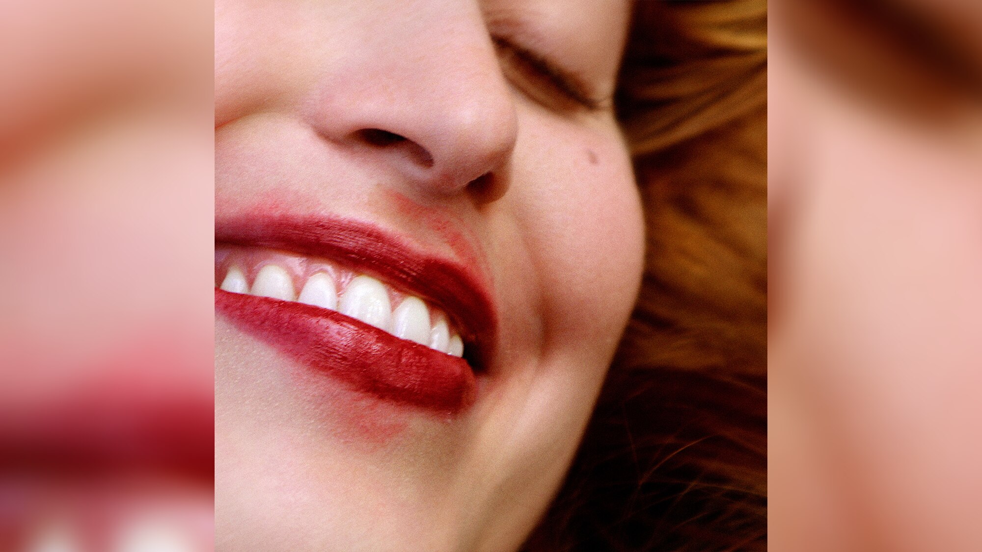 A close-up of a smiling woman in smudged red lip-stick, eyes closed, grinning.