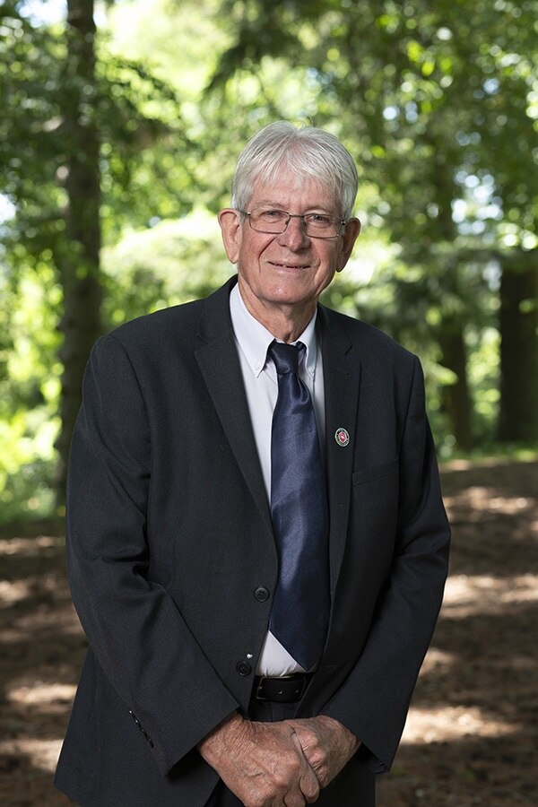 Un hombre mayor con gafas de pie en un traje sonriendo a la cámara.