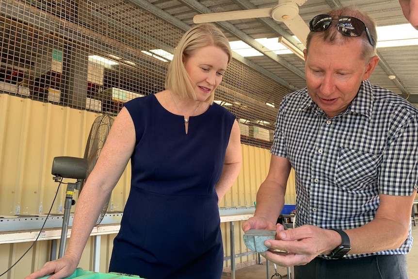NT Mining Minister Nicole Manison and a man looking at a piece of metal the man is lifting up from a table, inside a large shed.