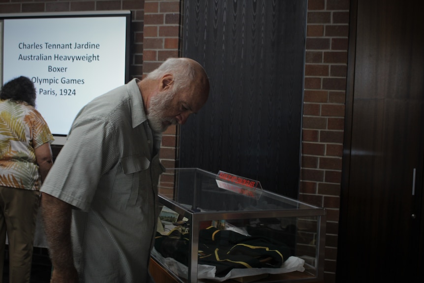 An elderly man looks at a table of artifacts 