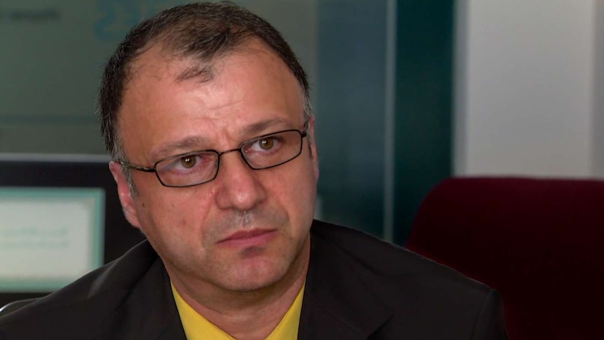 Mohammed Azimi, wearing suit, yellow shirt and tie, with glasses and thinning black hair, sits in office.