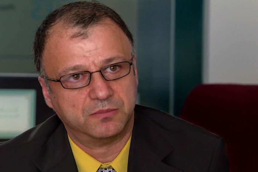 Mohammed Azimi, wearing suit, yellow shirt and tie, with glasses and thinning black hair, sits in office.