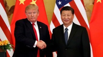 Donald Trump looks straight ahead with his lips pursed as he shakes Xi Jinping's hand, right, as he smiles into the camera.