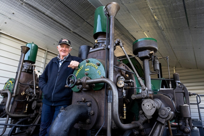 A photo of an elderly man and a century old engine in a shed.
