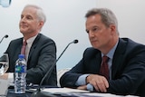 Rupert Hogg and John Slosar wear suits and sit in front of two microphones at a press conference