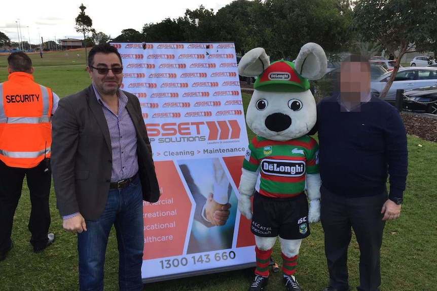 A man poses with a person in a rabbit suit and a green and red rugby jersey.