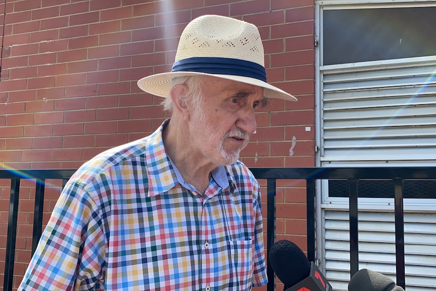 An elderly man wearing a check shirt and a hat
