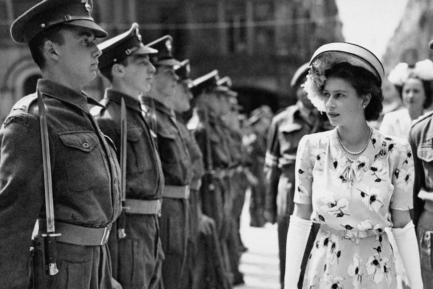 A black and white photograph of Princess Elizabeth in a hat and dress inspecting a row of soldiers.