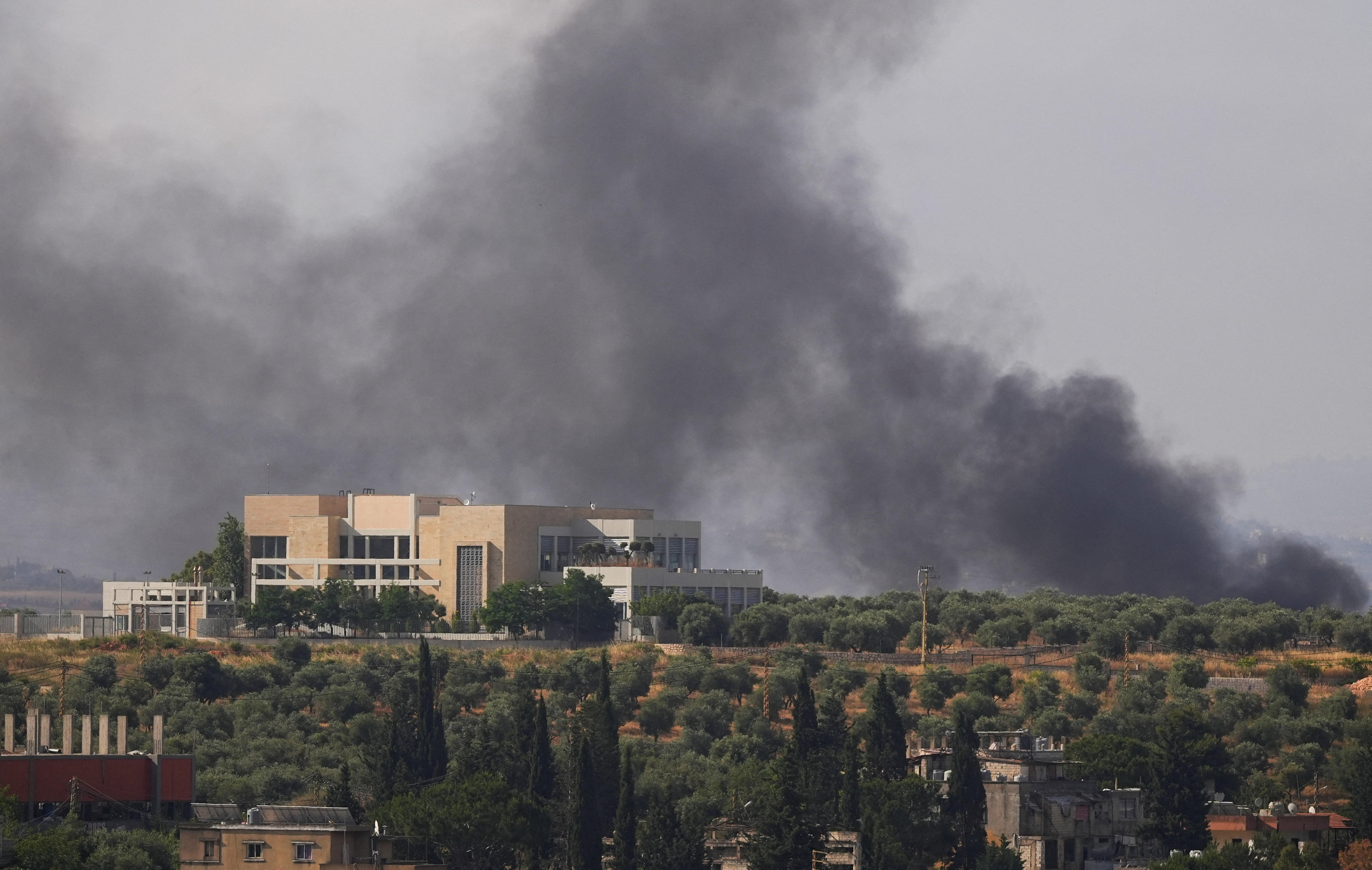 A building stands on the top of a hillside, with grey smoke rising behind it into the sky.