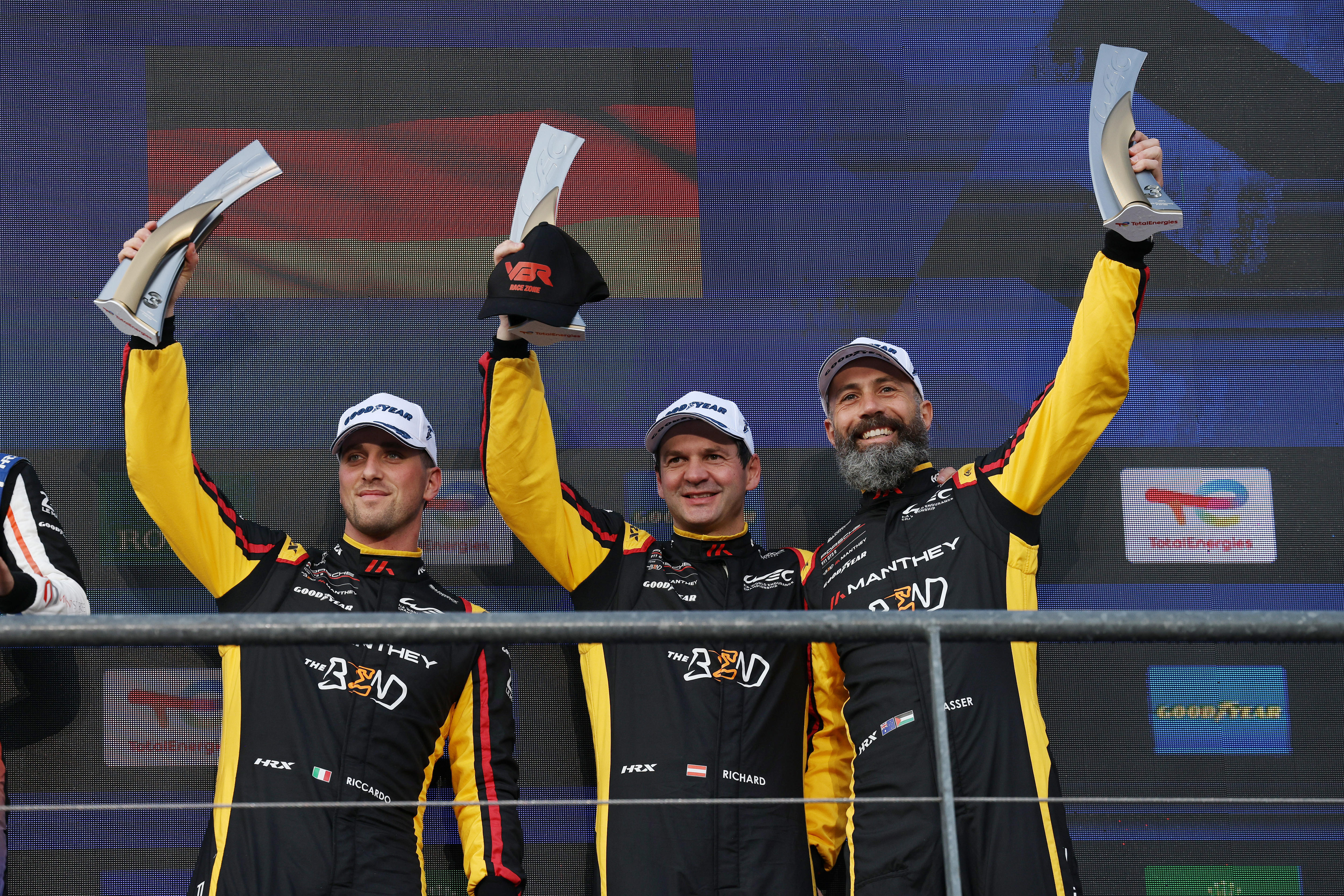 Three drivers holding up trophies on the podium after an endurance race