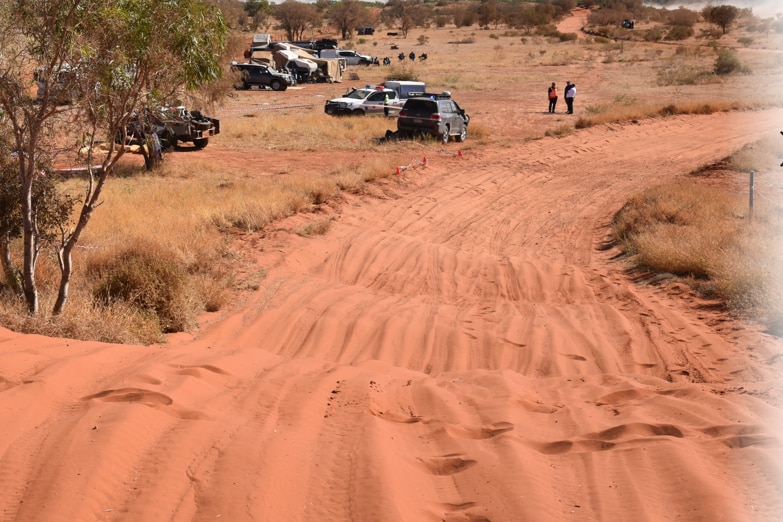 A sandy off-road track. Police vehicles are parked to the side.
